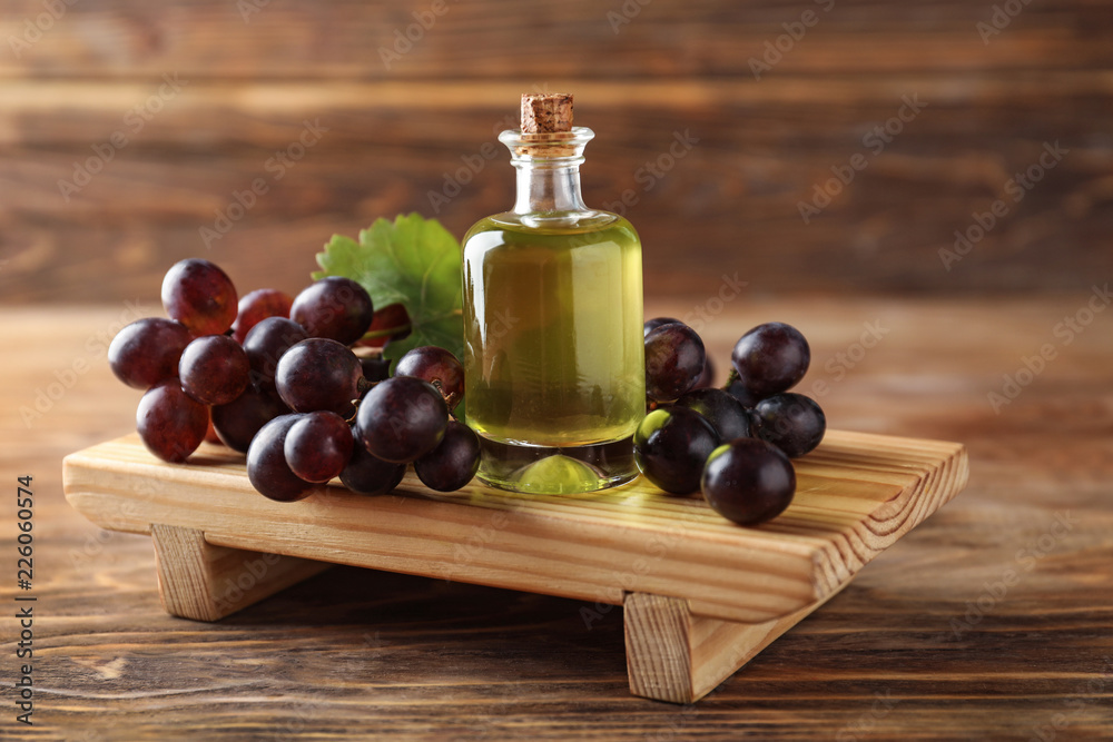 Bottle with oil and fresh grapes on wooden stand