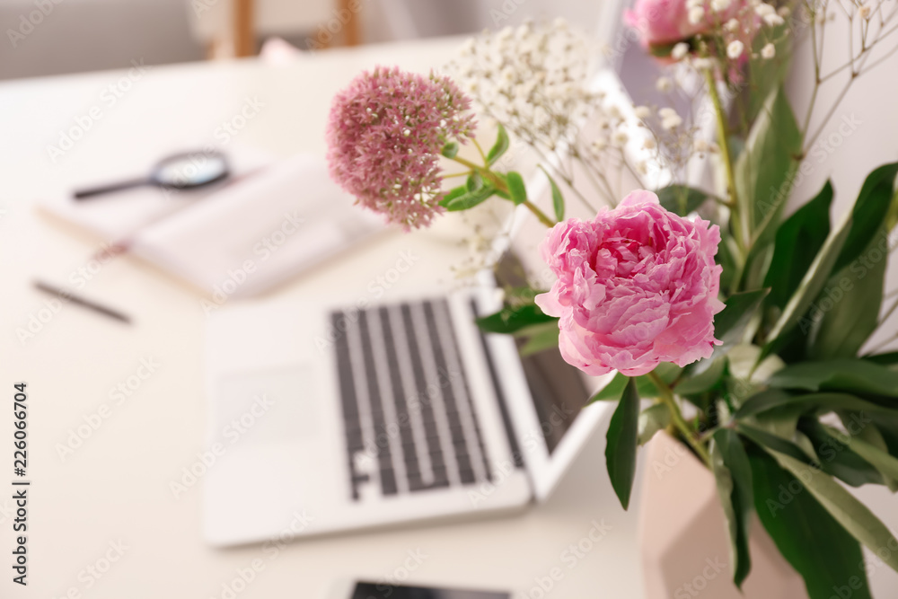 Vase with beautiful pink flowers and laptop on table