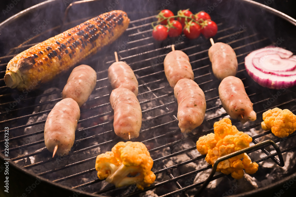 Cooking of tasty sausages and vegetables on barbecue grill, closeup