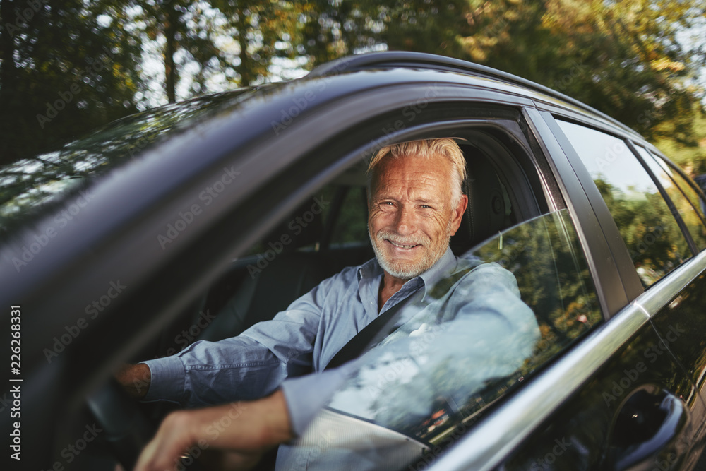 Smiling senior man driving along a road in the countryside