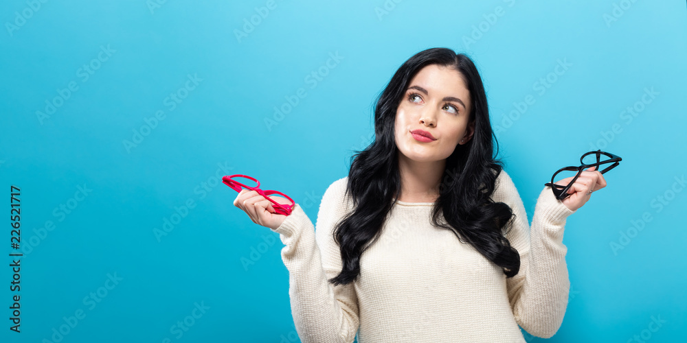 Young woman comparing two eye glasses on a blue background