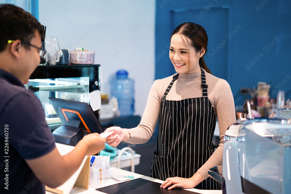 亚洲女咖啡师在咖啡店里接受顾客的信用卡。