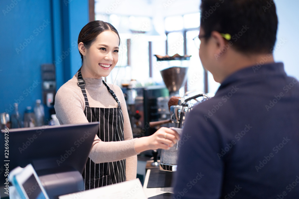 亚洲女咖啡师在咖啡店里接受顾客的信用卡。