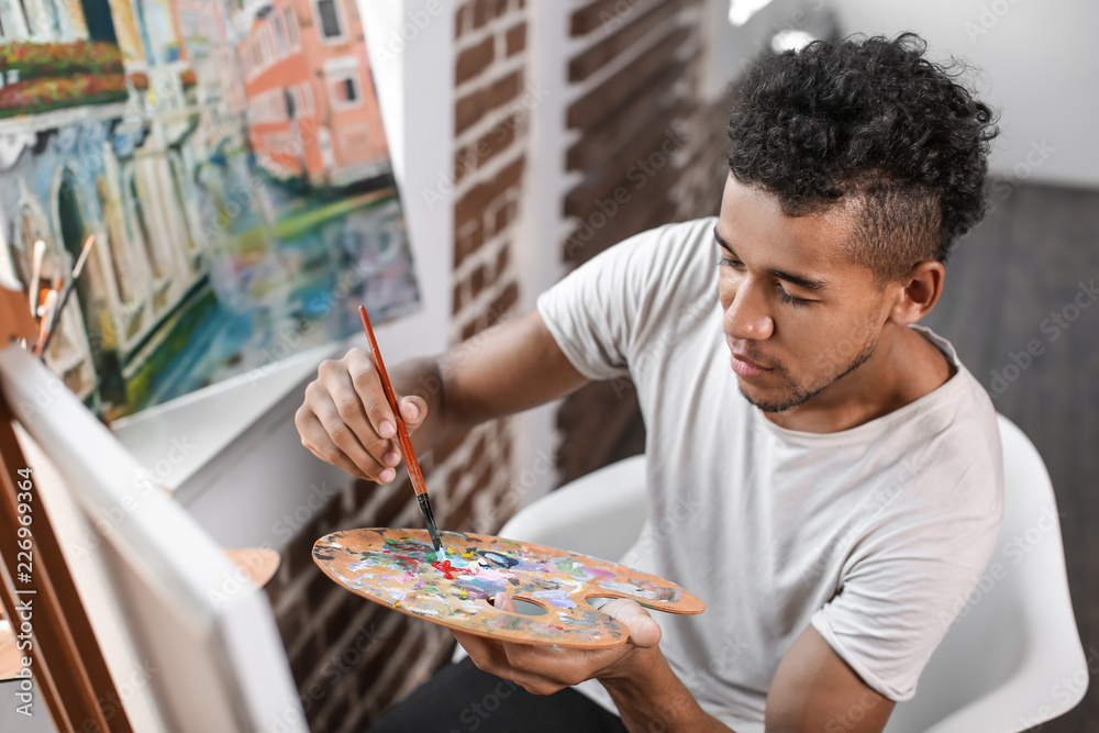 Young African-American artist painting picture in workshop