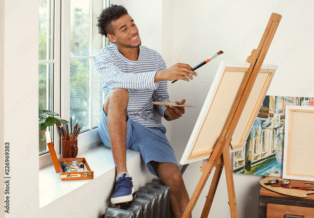 Young African-American artist painting picture at home