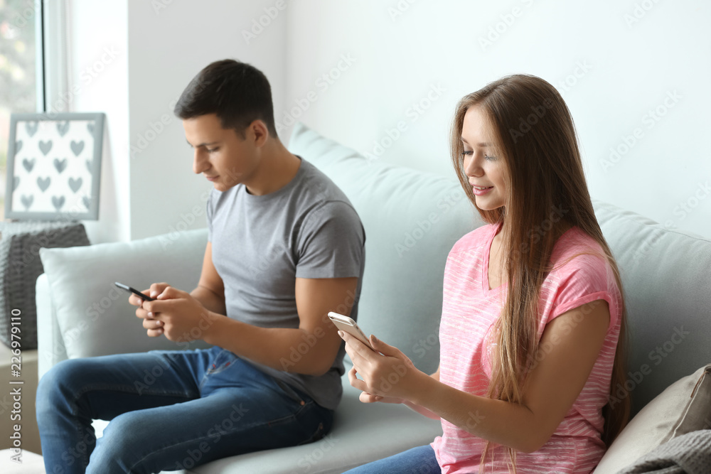 Young couple with mobile phones sitting on sofa at home