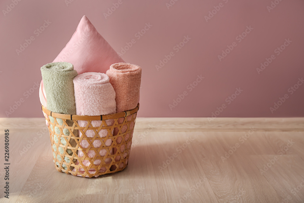 Laundry basket with clean towels and pillow on floor near color wall