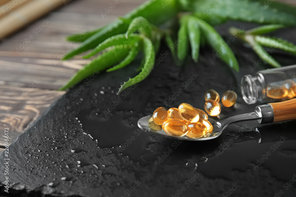 Spoon with pills and fresh aloe vera on slate plate, closeup