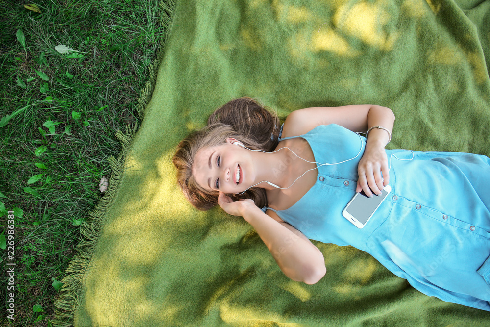 Beautiful young woman listening to music while lying on green grass outdoors