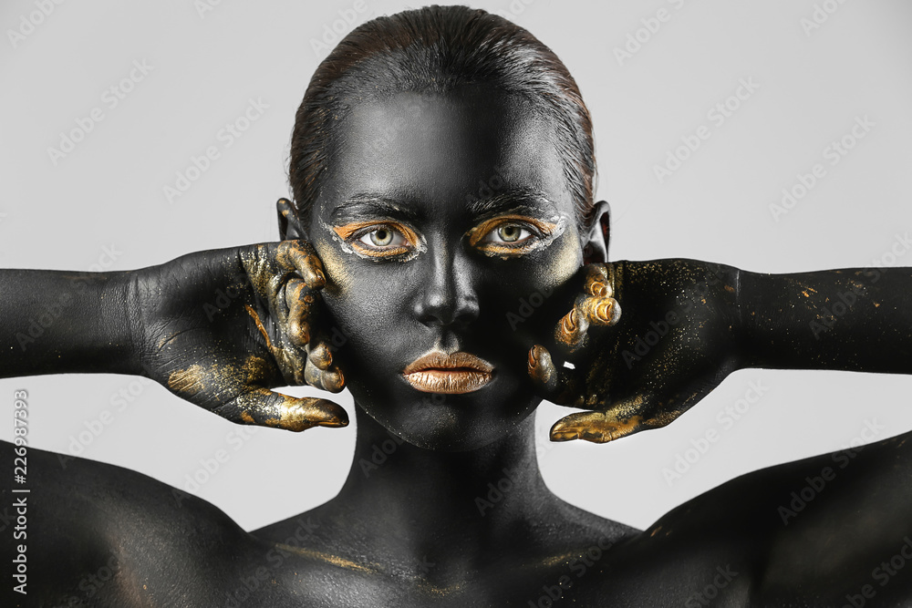 Beautiful woman with black and golden paint on her body against light background