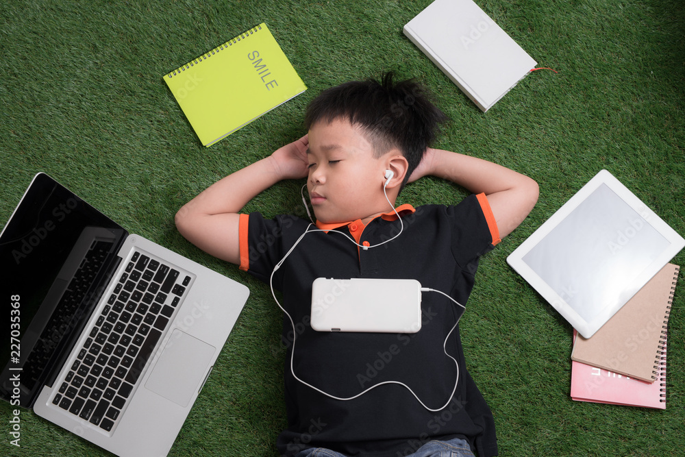 Little boy lying on the grass and listening music with headphones