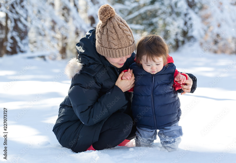 蹒跚学步的男孩和妈妈在雪地里玩耍