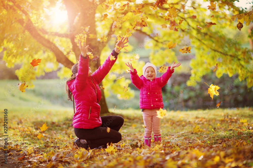 Mother playing with daughter on sunny day in autumn. Woman with a child on yellow foliage background