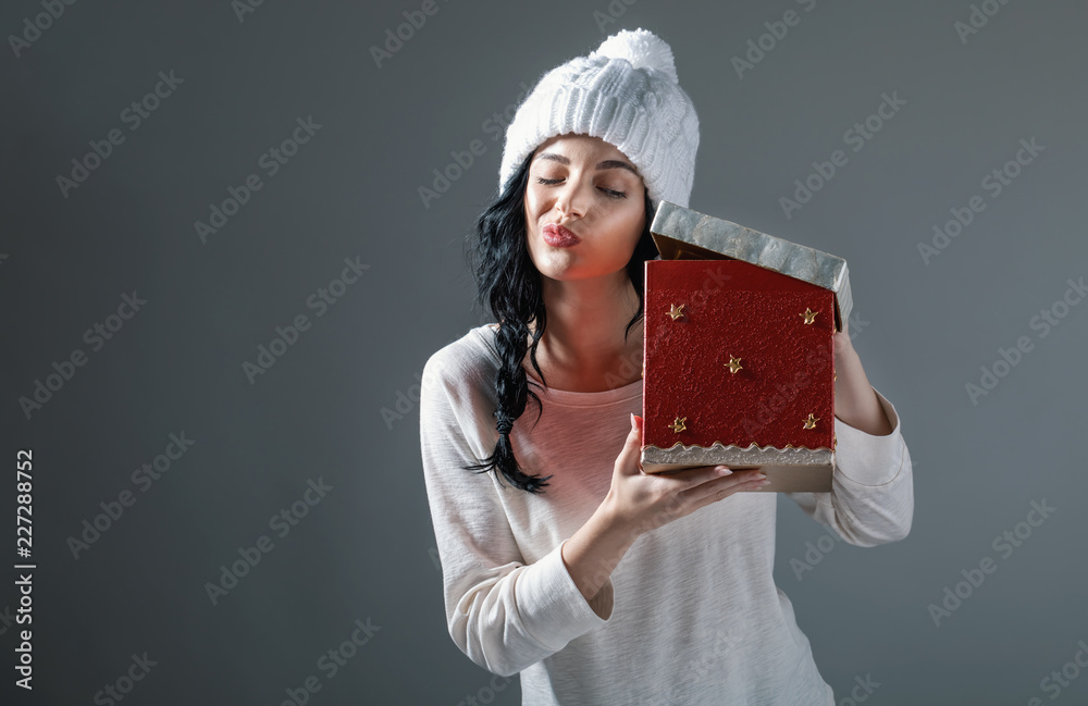 Young woman opening a Christmas present box on a gray background