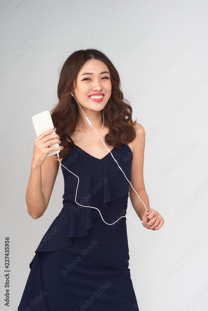 Happy carefree young woman dancing and listening to music from smartphone over grey background