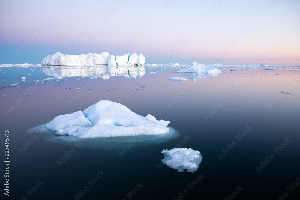 Early morning summer alpenglow lighting up icebergs during midnight season. Ilulissat, Greenland.