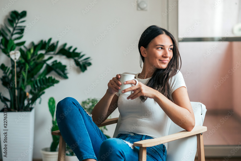 漂亮的年轻女人在家喝茶。把目光移开。