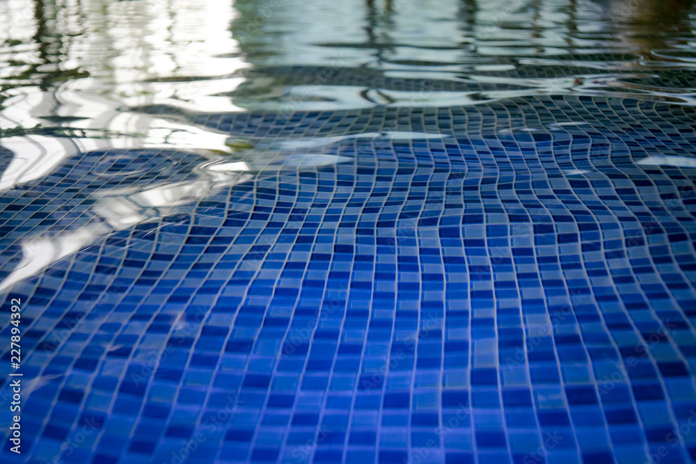 The azur mosaic bottom of an aquapark pool. A view to the tiled floor through the clean water of ind