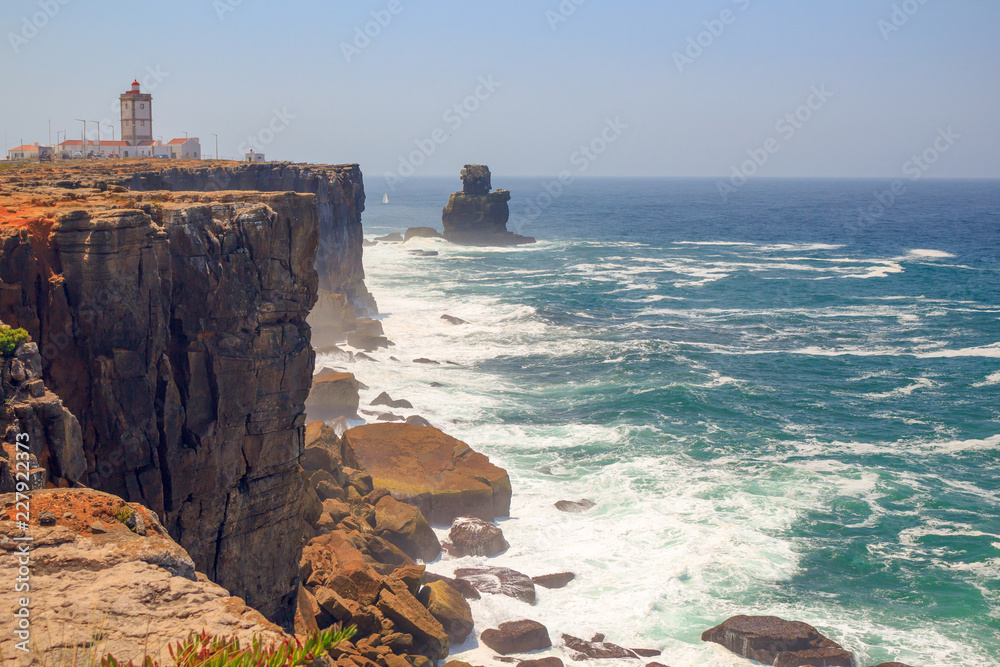 阳光明媚的日子里，岩石海岸、海浪和灯塔的全景。波图加海滨小镇佩尼切