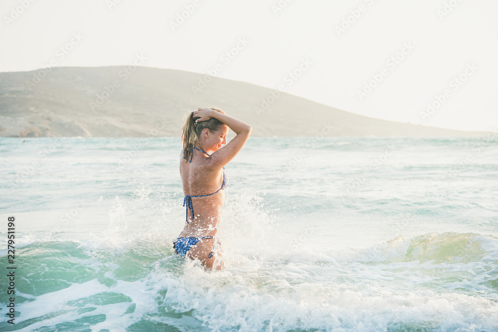 穿着泳衣的年轻金发美女游客站在地中海的波浪水中放松