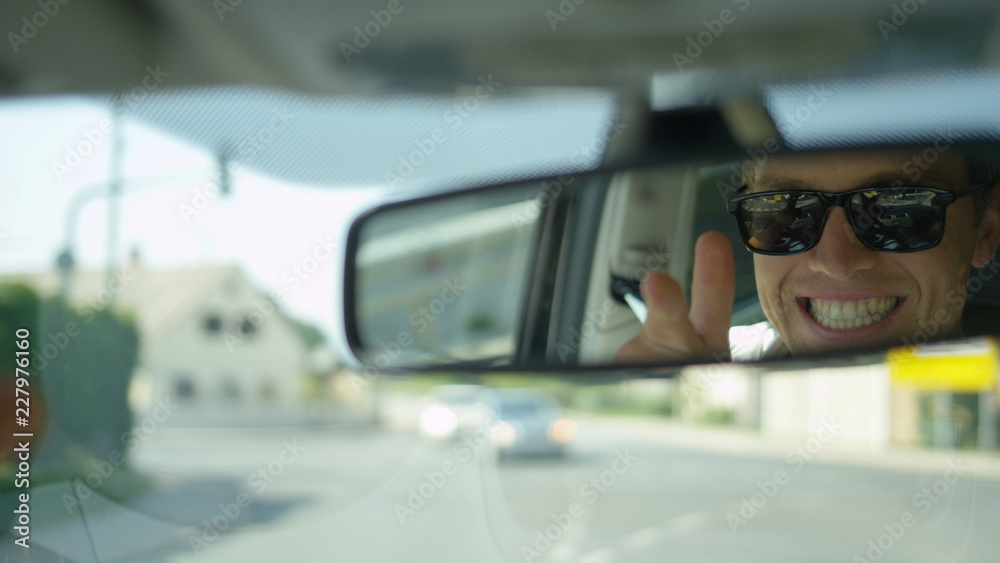 CLOSE UP: Young male driver adjust his rear view mirror and looks at himself.