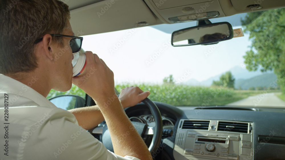 CLOSE UP: Young man drinking a fresh cup of coffee while driving through country