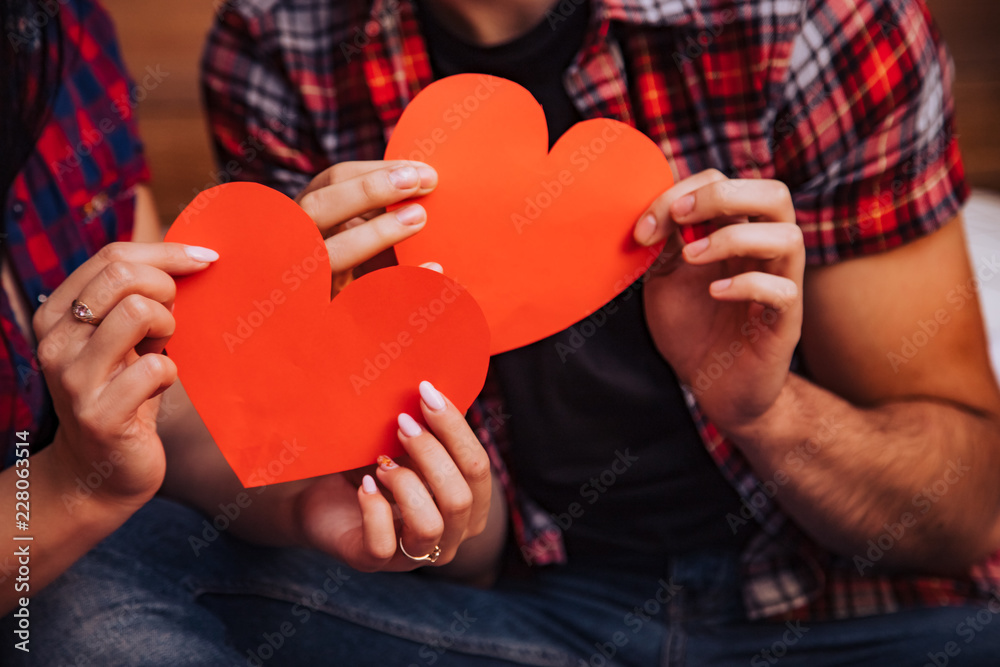 a man and a woman hold in their hands paper hearts of red color on the day of Saint Valentine. Close