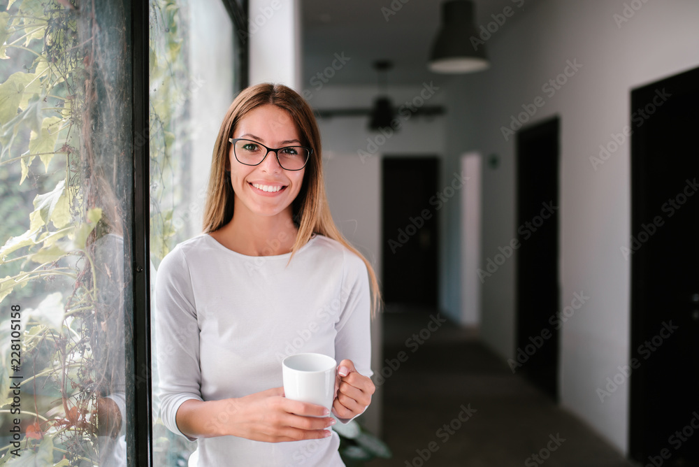 室内拿着马克杯微笑的年轻女子的肖像。