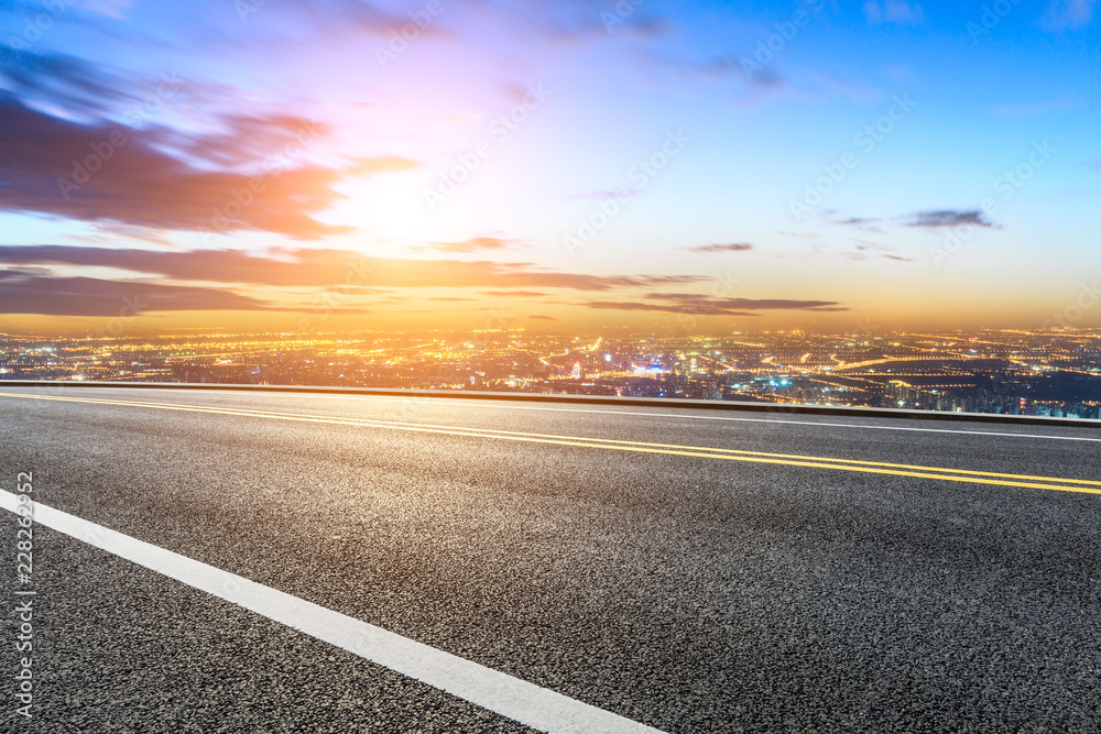 Modern city skyline and buildings with empty asphalt road at sunset