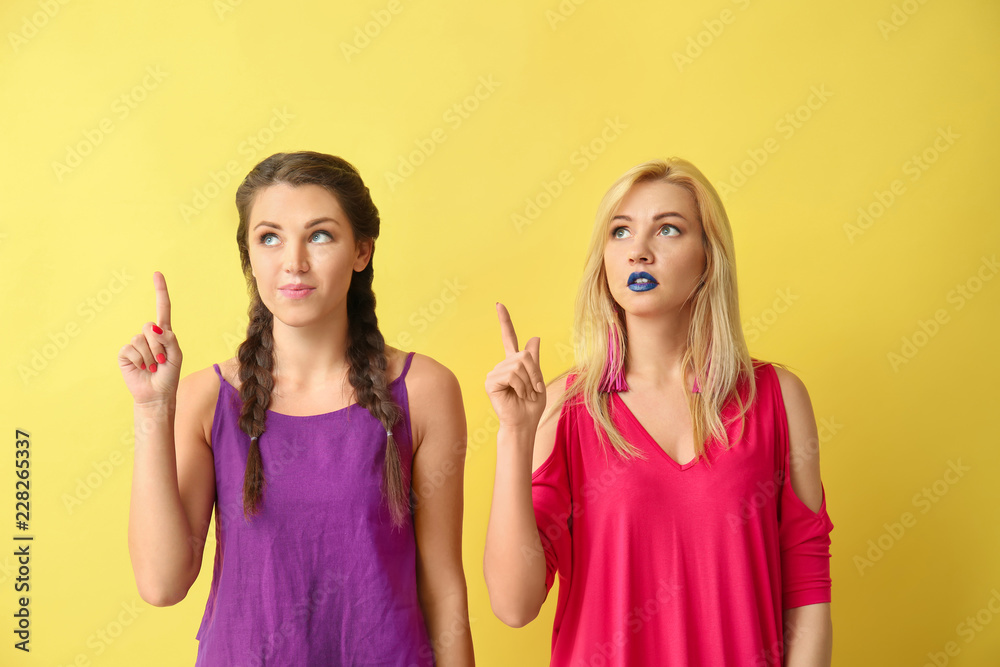 Portrait of beautiful women with raised index fingers on color background