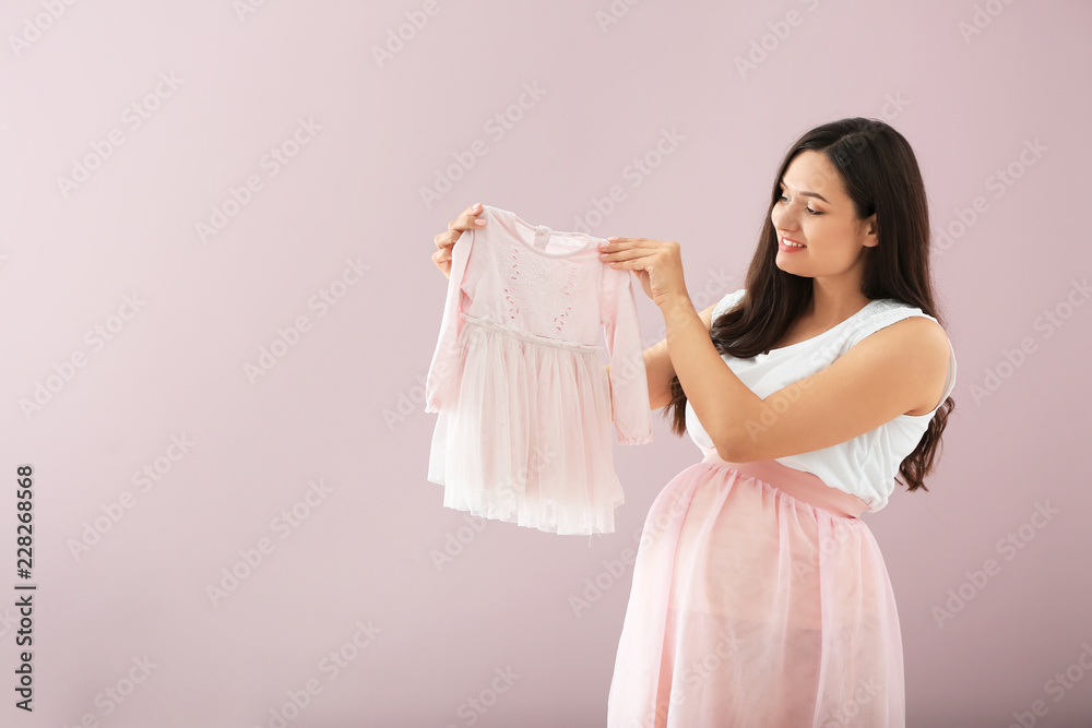 Beautiful pregnant woman with baby dress on color background