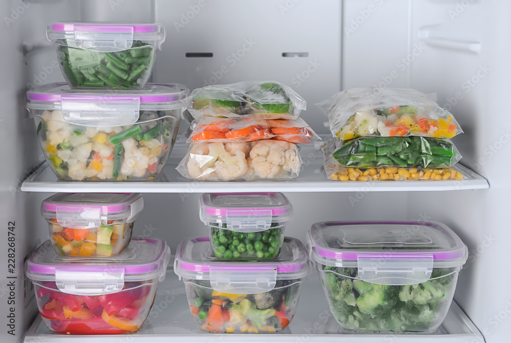 Containers and plastic bags with frozen vegetables in refrigerator