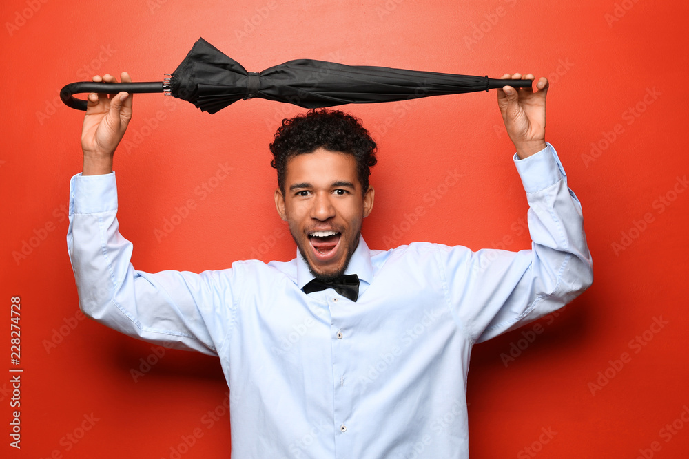 Portrait of happy African-American man with umbrella on color background