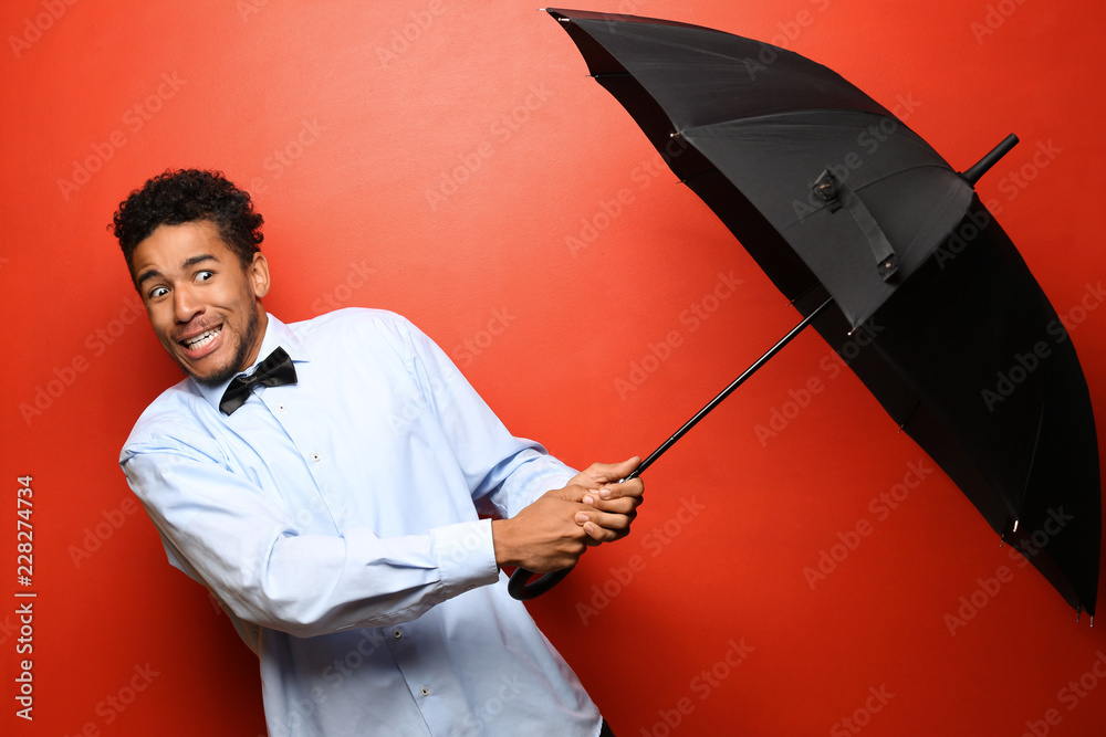 Portrait of scared African-American man with umbrella on color background