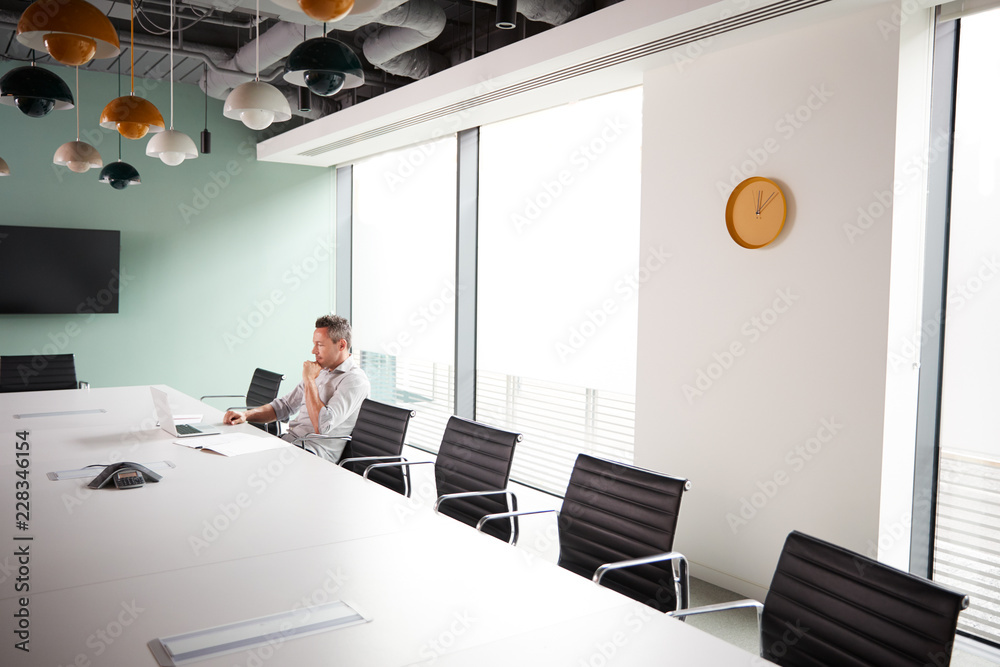 Casually Dressed Mature Businessman Working On Laptop At Boardroom Table In Meeting Room