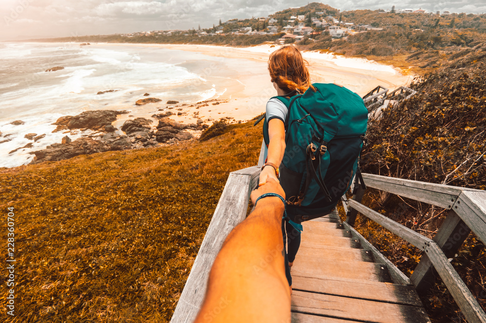 Woman with backpack holding man by hand going to Australia coastline