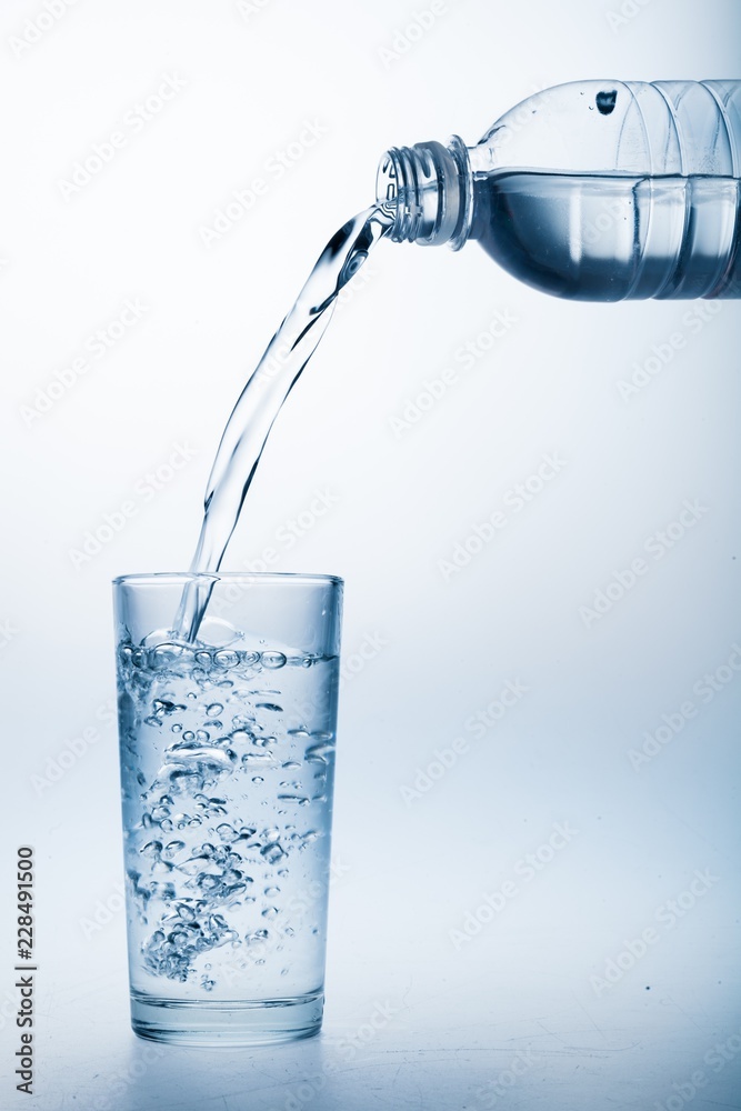 Pouring Water from Bottle into Glass on the Blue Background