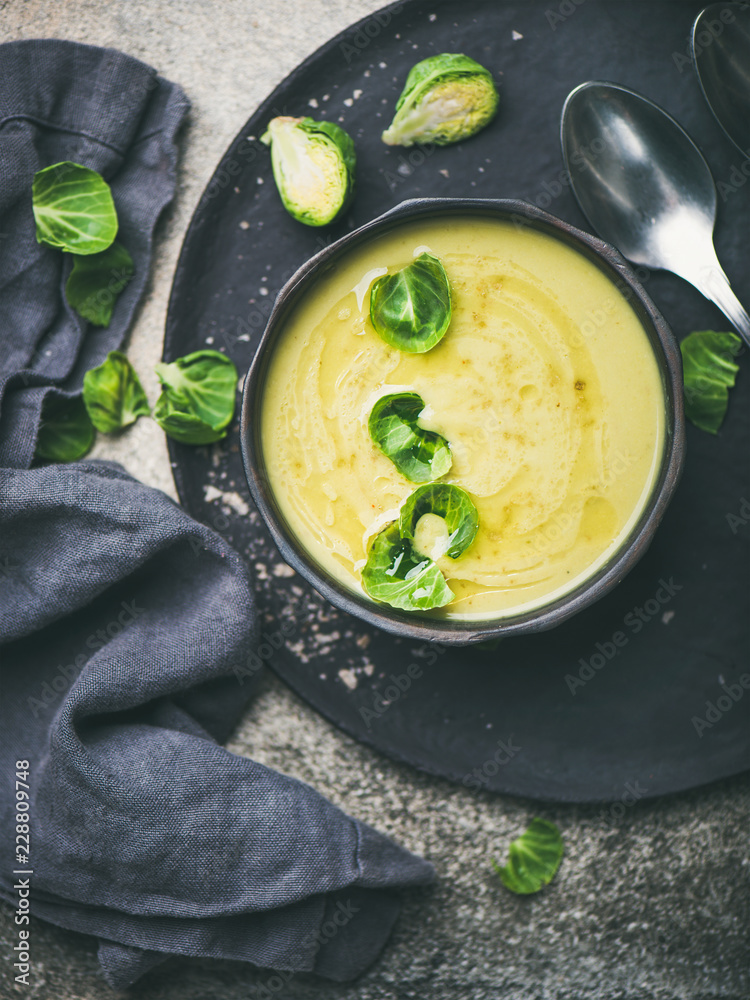 Seasonal brussels sprouts vegetable cream soup in black bowl and fresh green brussel sprouts over bl