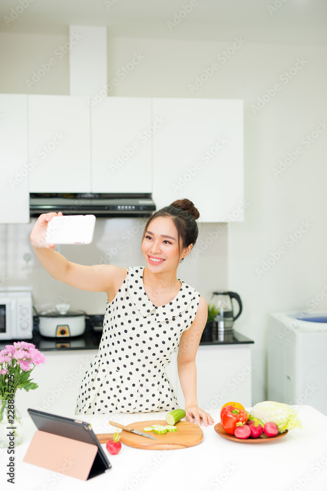 Young pretty woman using smart phone while cooking in kitchen