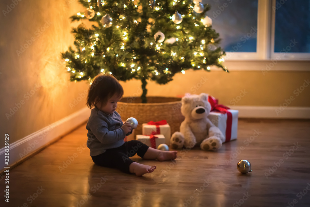 Toddler boy playing under the Christmas tree at night