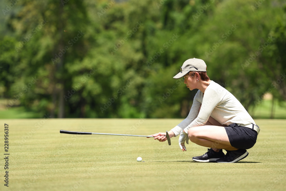 Woman golfer check line for putting golf ball on green grass