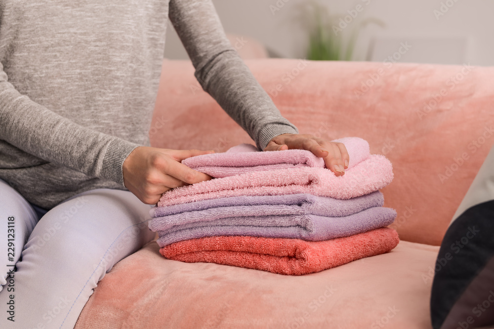 Woman folding clean soft towels on sofa at home