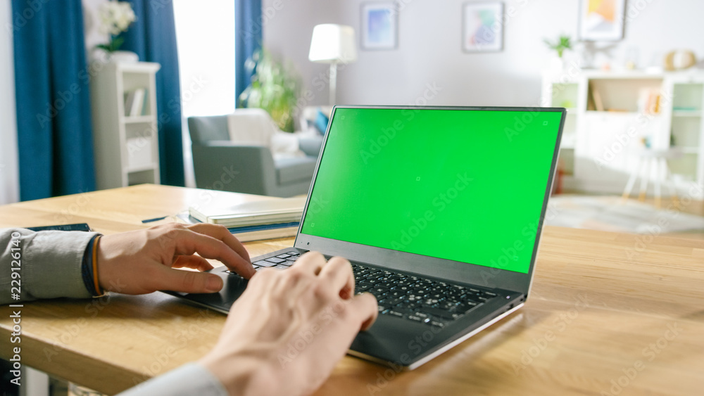 Close-up of a Man Uses Laptop with Green Mock-up Screen While Sitting at the Desk in His Cozy Living