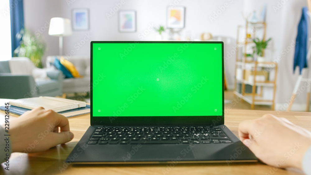 First Person Close-up Shot Man Uses Laptop with Green Mock-up Screen While Sitting at the Desk in Hi