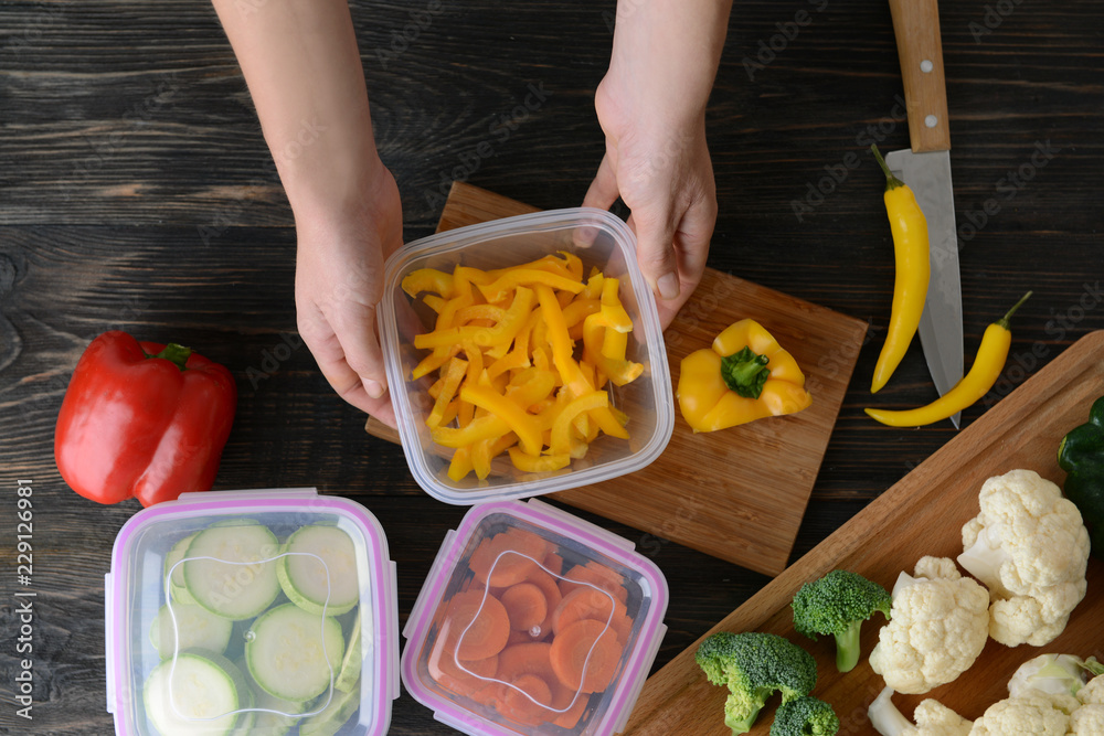 Woman holding plastic container with fresh pepper for freezing on wooden table