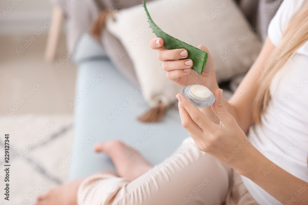 Beautiful young woman using cream with aloe vera extract at home