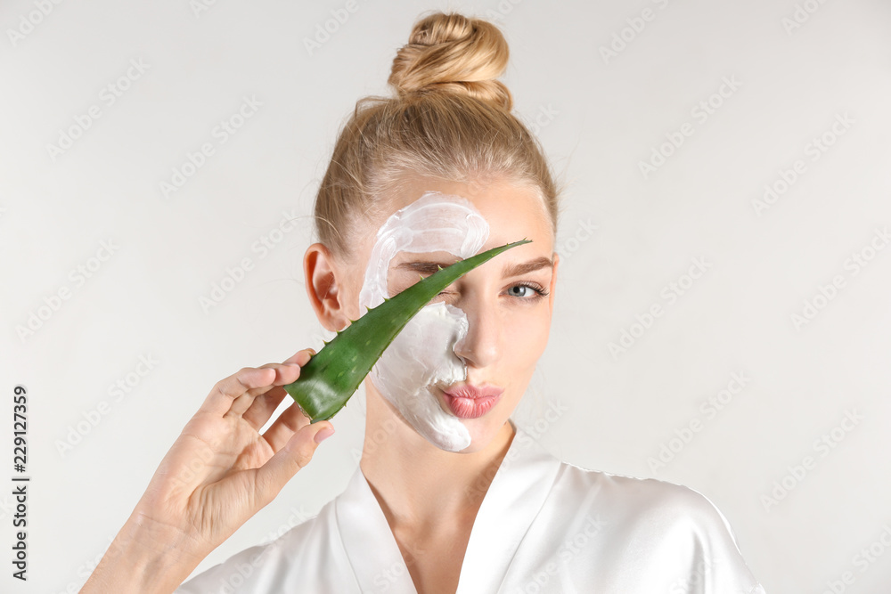 Beautiful young woman with facial mask containing aloe vera extract, on light background