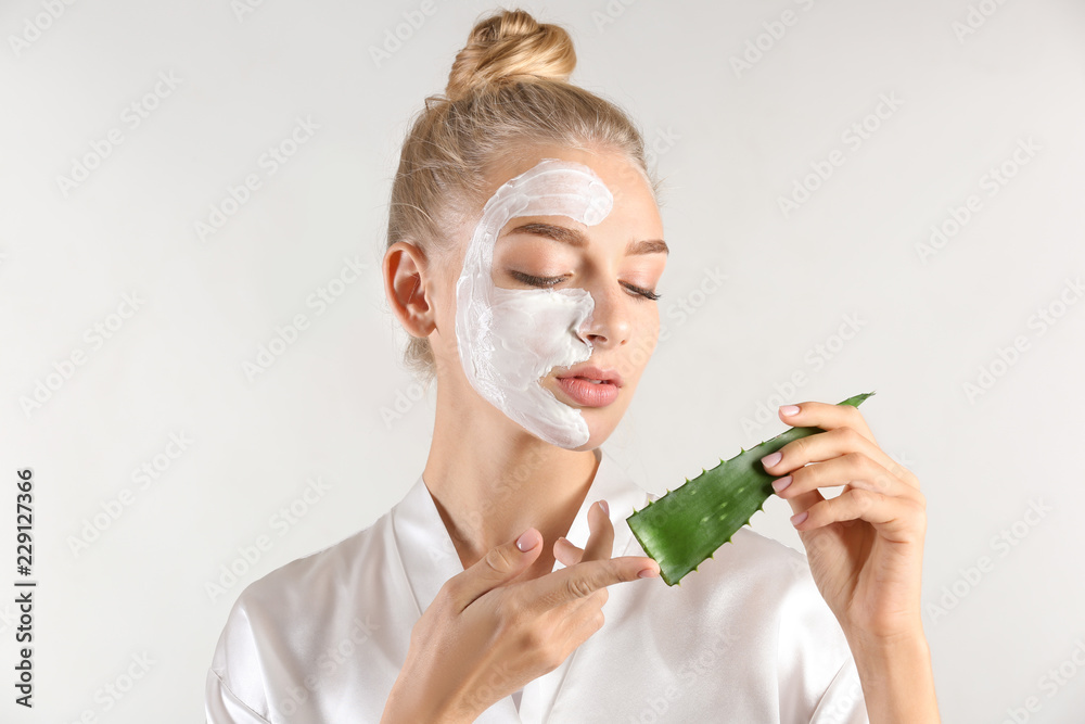 Beautiful young woman with facial mask containing aloe vera extract, on light background