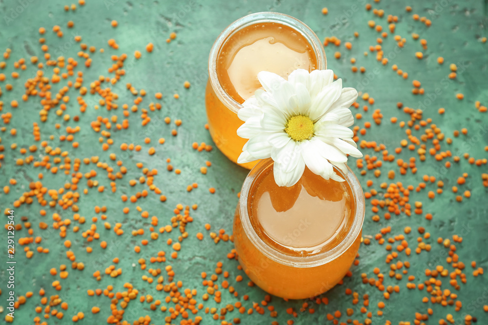 Jars of honey and flower on color background