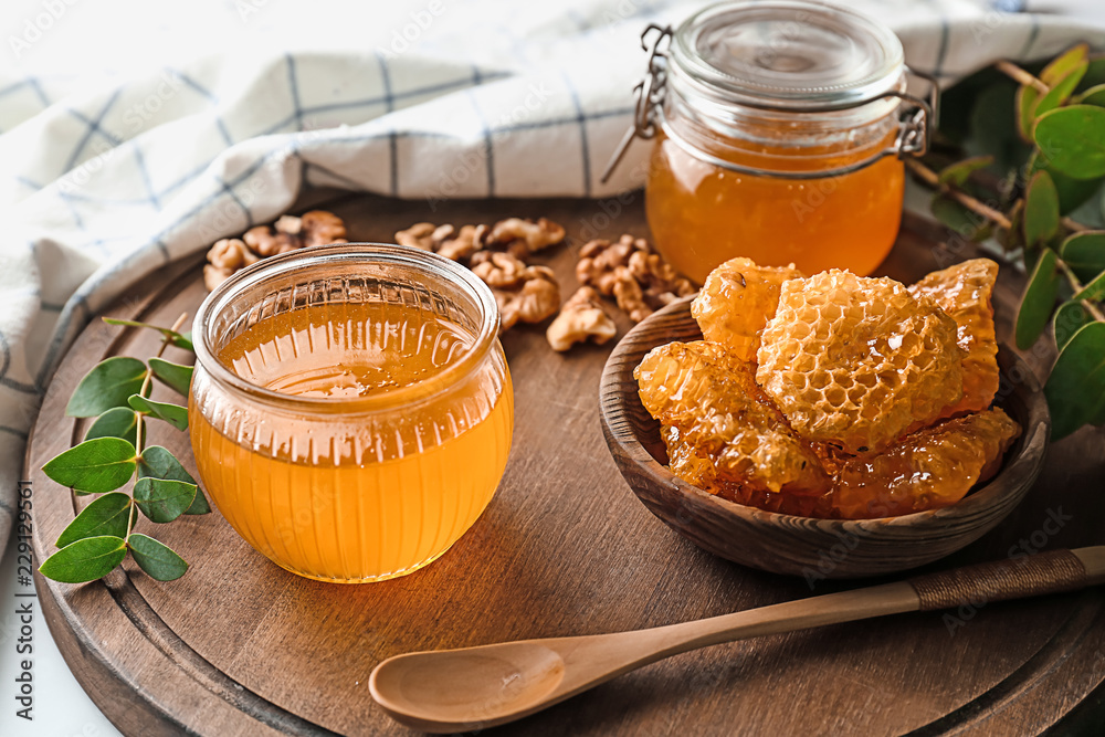 Bowl with honeycomb and  jars of honey on wooden board